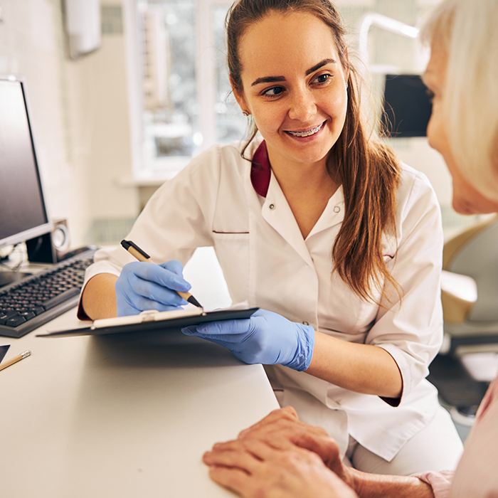 Dental team member writing on a clipboard while talking to a patient