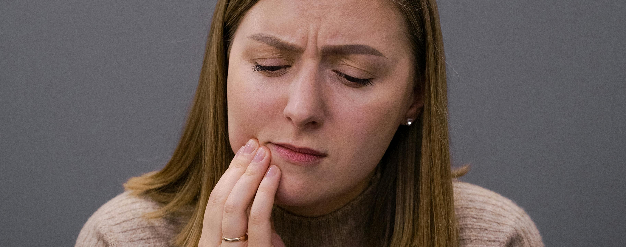 Woman holding her jaw in pain before seeing an emergency dentist in Sterling Heights