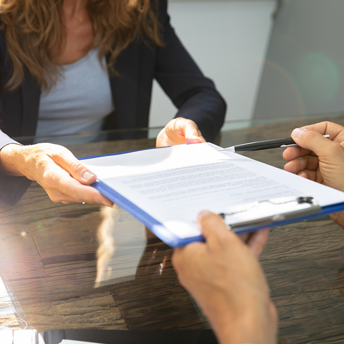 Perosn handing a clipboard to someone across a desk