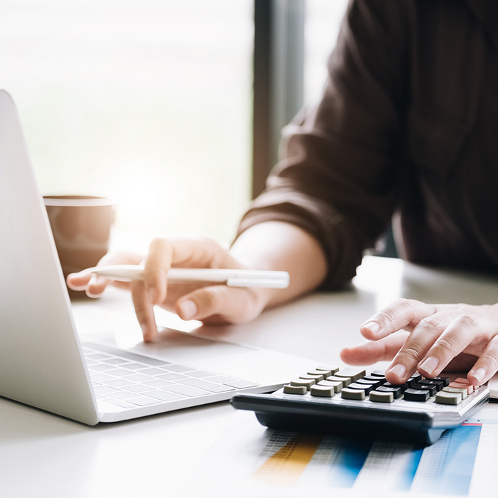 Person at a desk typing on a calculator and a laptop