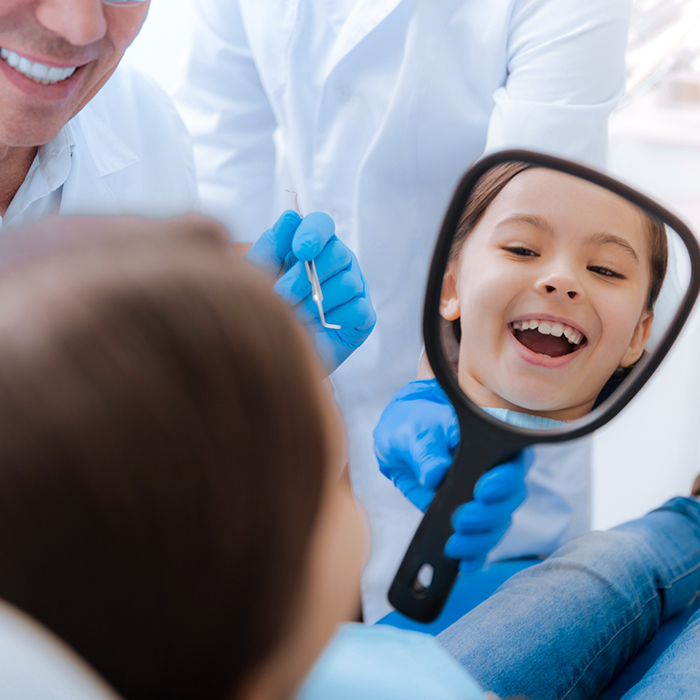 Young girl in the dental chair looking at her smile in a mirror